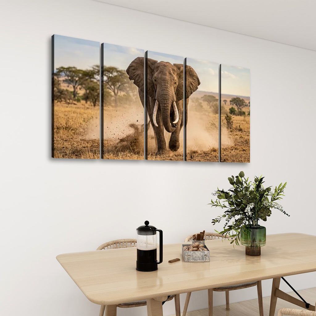 A five-panel canvas wall art set depicting a large elephant walking through a dry grass savanna, displayed on a white wall above a light wood dining table with a plant and coffee press.