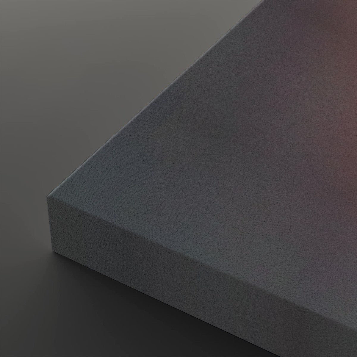 A close-up studio shot of a matte gray rectangular block or panel corner, shown against a matching dark gray background with soft warm light on the top surface.