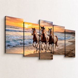 A five-panel canvas wall art set depicting three horses running along a sandy beach at sunset, mounted on a light beige wall.