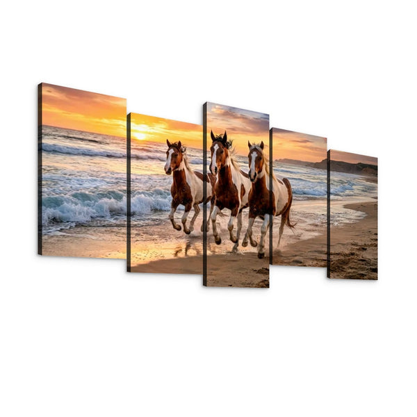Five-panel canvas wall art showing three horses running along a sandy beach at sunset, with ocean waves and a warm orange sky.