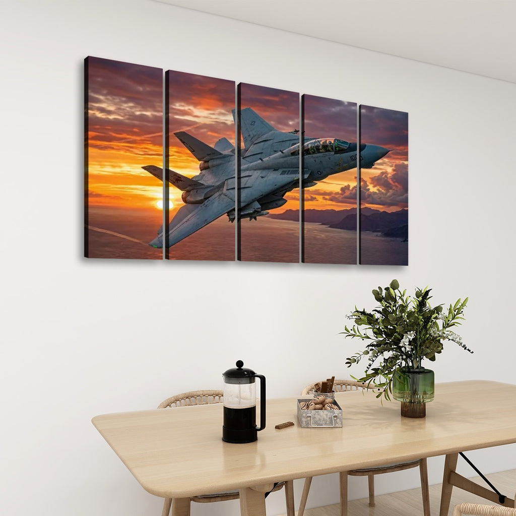 A five-panel canvas wall art set depicting a gray Grumman F-14 fighter jet flying across a dramatic orange and purple sunset sky, displayed on a white wall above a dining table with chairs, a plant, and a French press.