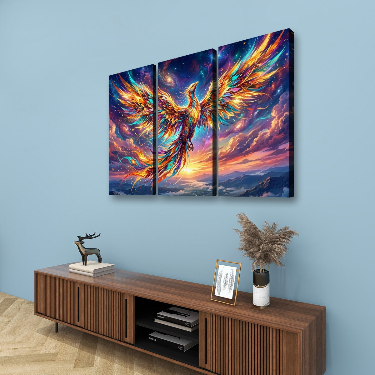 A three-panel canvas wall art set depicting a glowing phoenix with fiery orange, yellow, blue, and purple wings against a dramatic sky, displayed above a wooden console in a styled room.