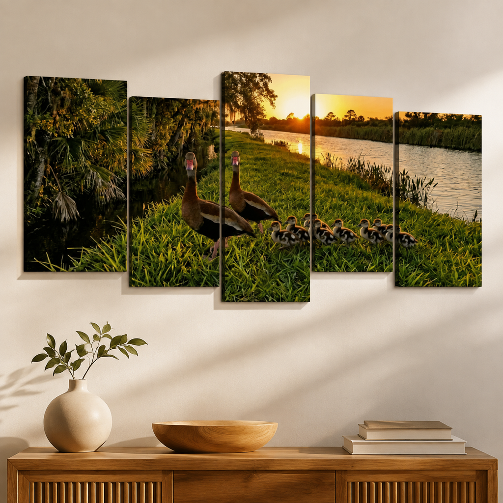 A five-panel canvas wall art set depicting a mother duck and her ducklings by a lake at sunset, displayed on a wall above a wooden console table with a vase and books.