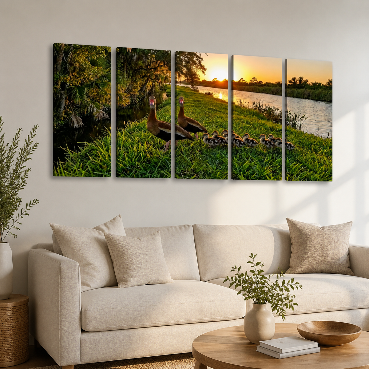 A five-panel canvas wall art set depicting a family of ducks and ducklings at sunset by a lake, displayed on a white wall above a beige sofa in a modern living room setting.