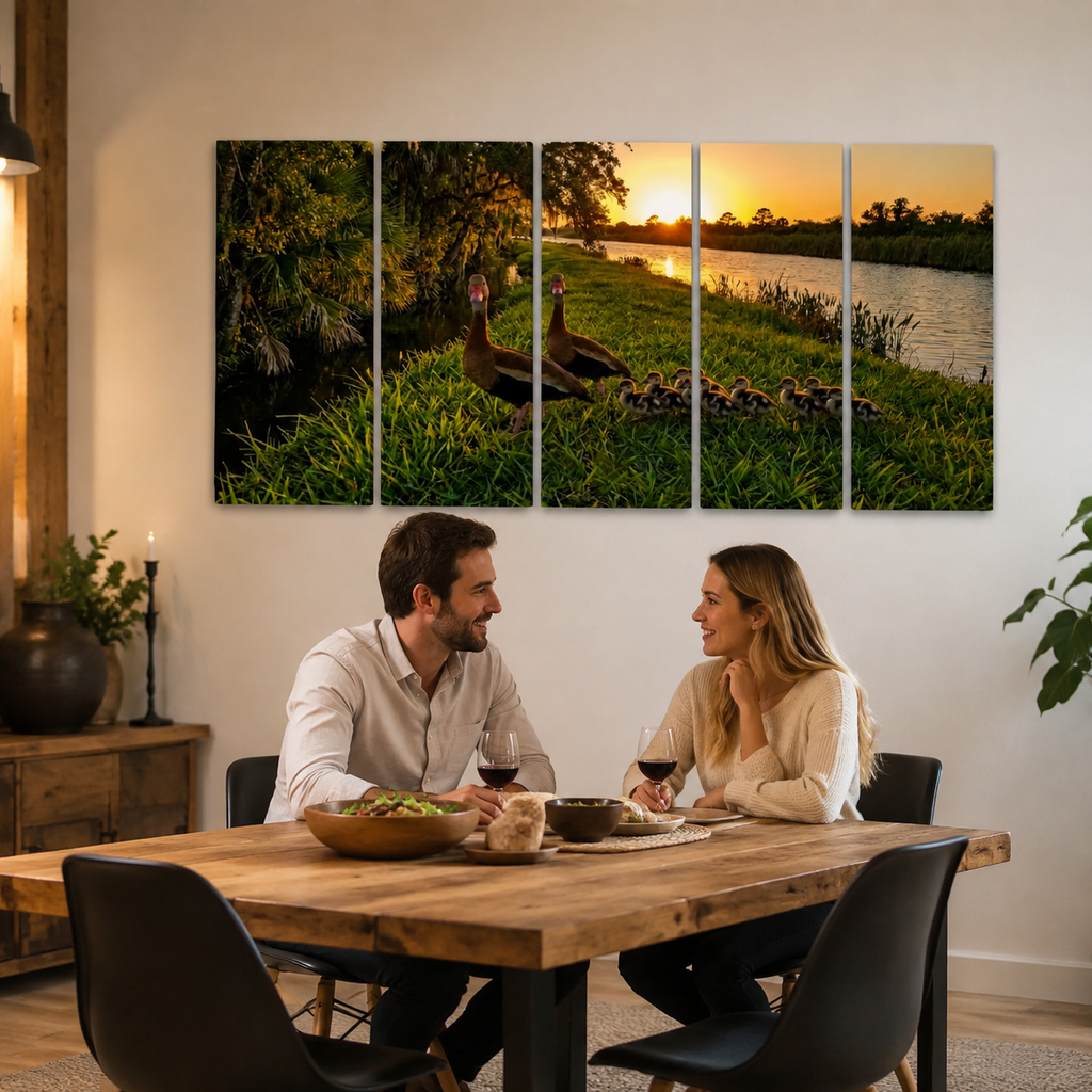 A five-panel canvas wall art set depicting a sunset scene with  Black-bellied Whistling-Ducks and ducklings by a lake, displayed on a wall above a dining table where a couple is seated and eating.
