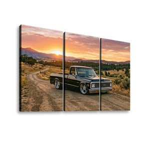 A three-panel canvas wall art print showing a black vintag 1970 Chevy C10 Fleetsidee pickup truck parked on a dirt road at sunset, with mountains and warm clouds in the background.