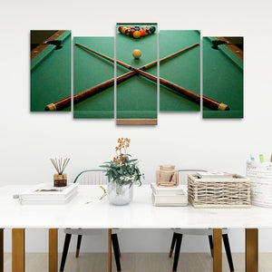 A 5-panel canvas wall art set depicting a green pool table with crossed pool cues and a billiard ball, displayed above a white dining table with decorative items in a modern room setting.