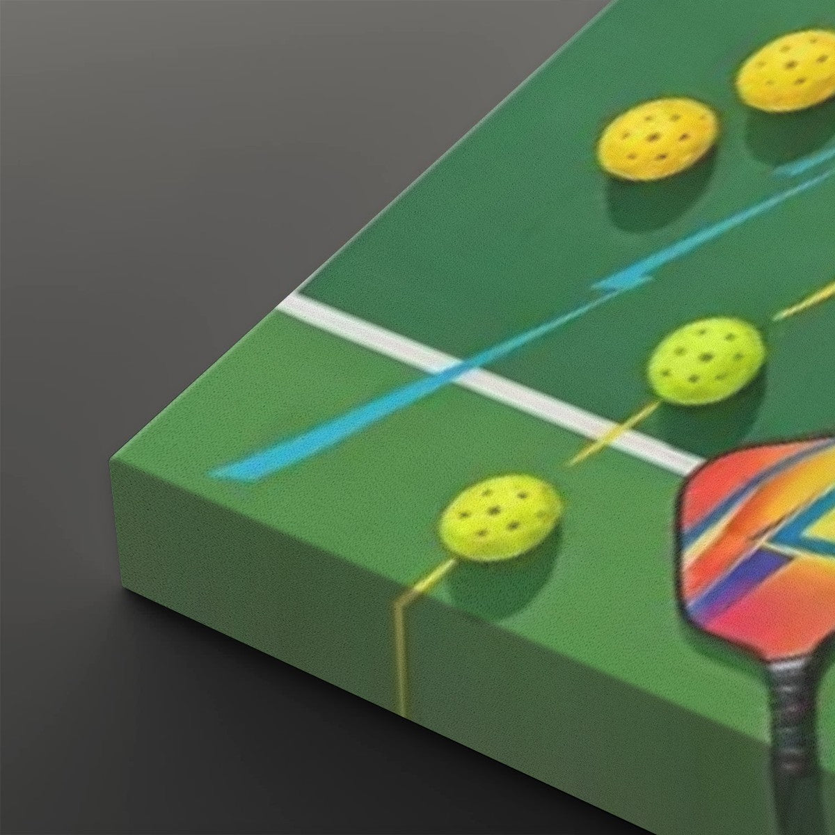 A close-up of a green table tennis court print or panel, showing yellow ping-pong balls, a white net line, blue motion lines, and part of a colorful paddle on a dark gray background.