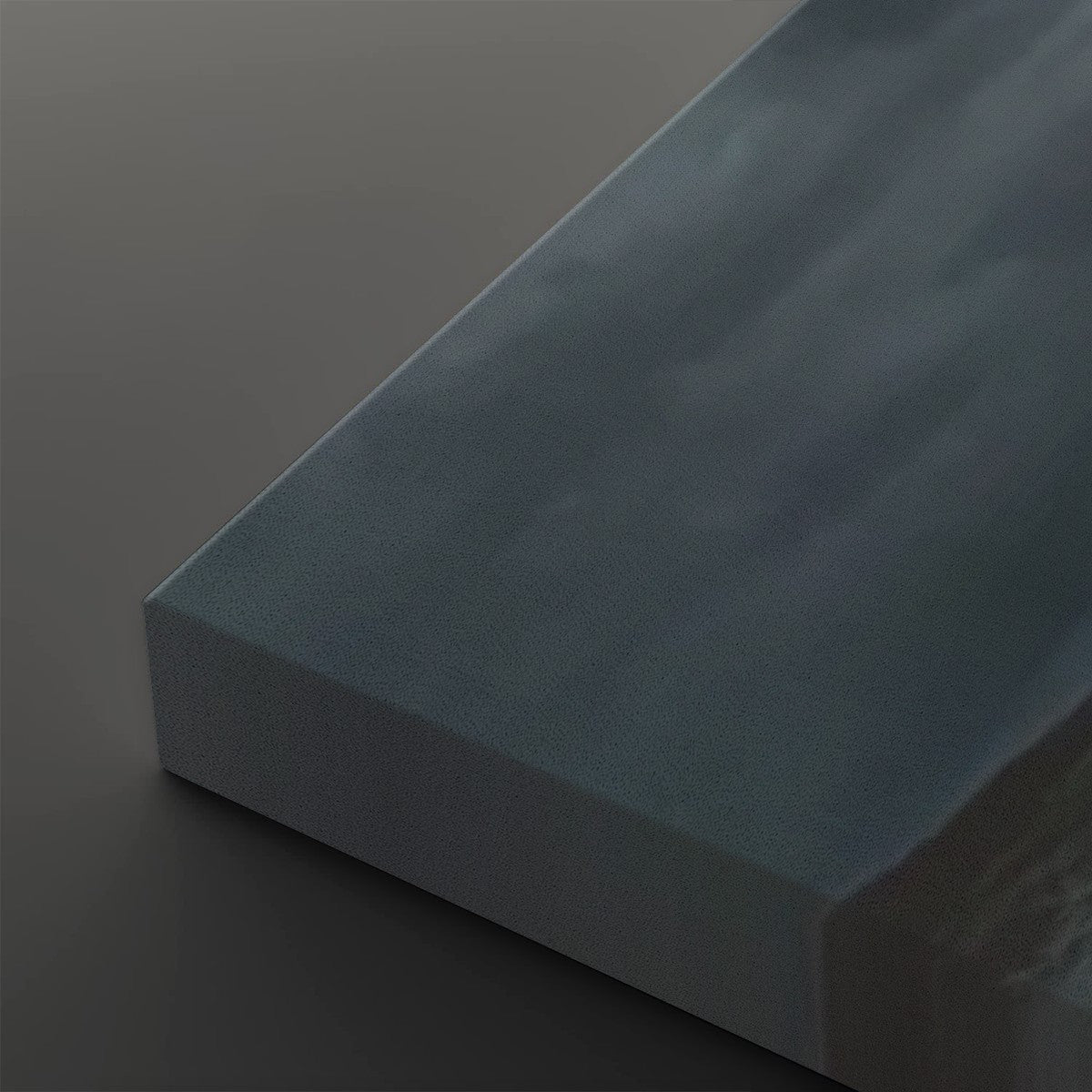 A close-up of a rectangular block of matte dark blue-gray material, showing its textured surface and angled edges against a dark gray background.