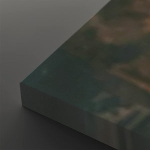 A close-up of a rectangular panel or board shown at an angle, with a dark teal-green top surface and a gray side edge, photographed against a dark gray background.