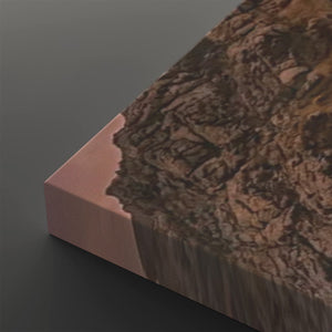 A close-up of a rectangular canvas or print showing a textured brown and tan rocky landscape with a pinkish edge, photographed on a dark gray background.