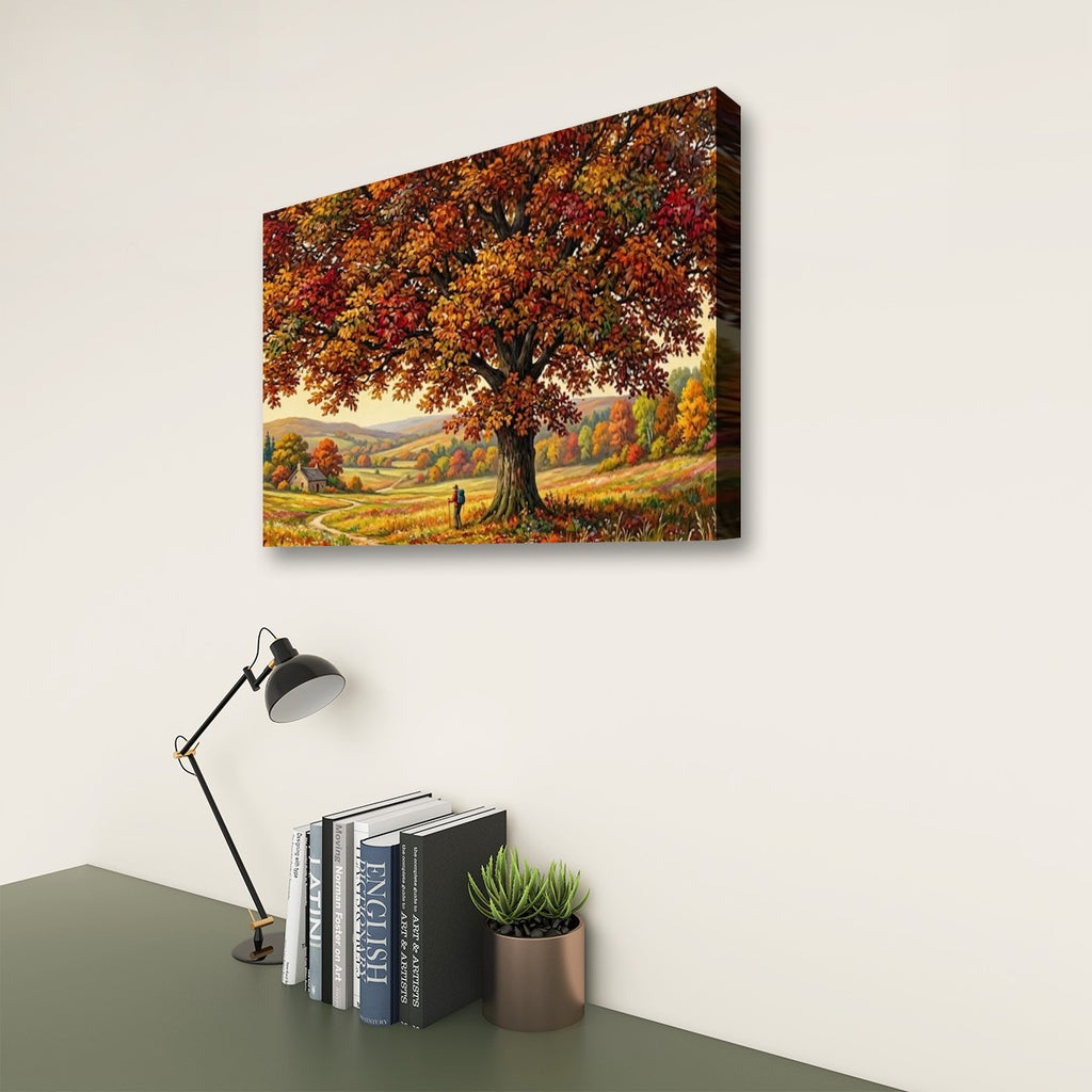 A rectangular wall art print showing a large autumn tree with orange and yellow foliage over a rolling landscape, displayed on a light wall above a desk with books, a lamp, and a small plant.
