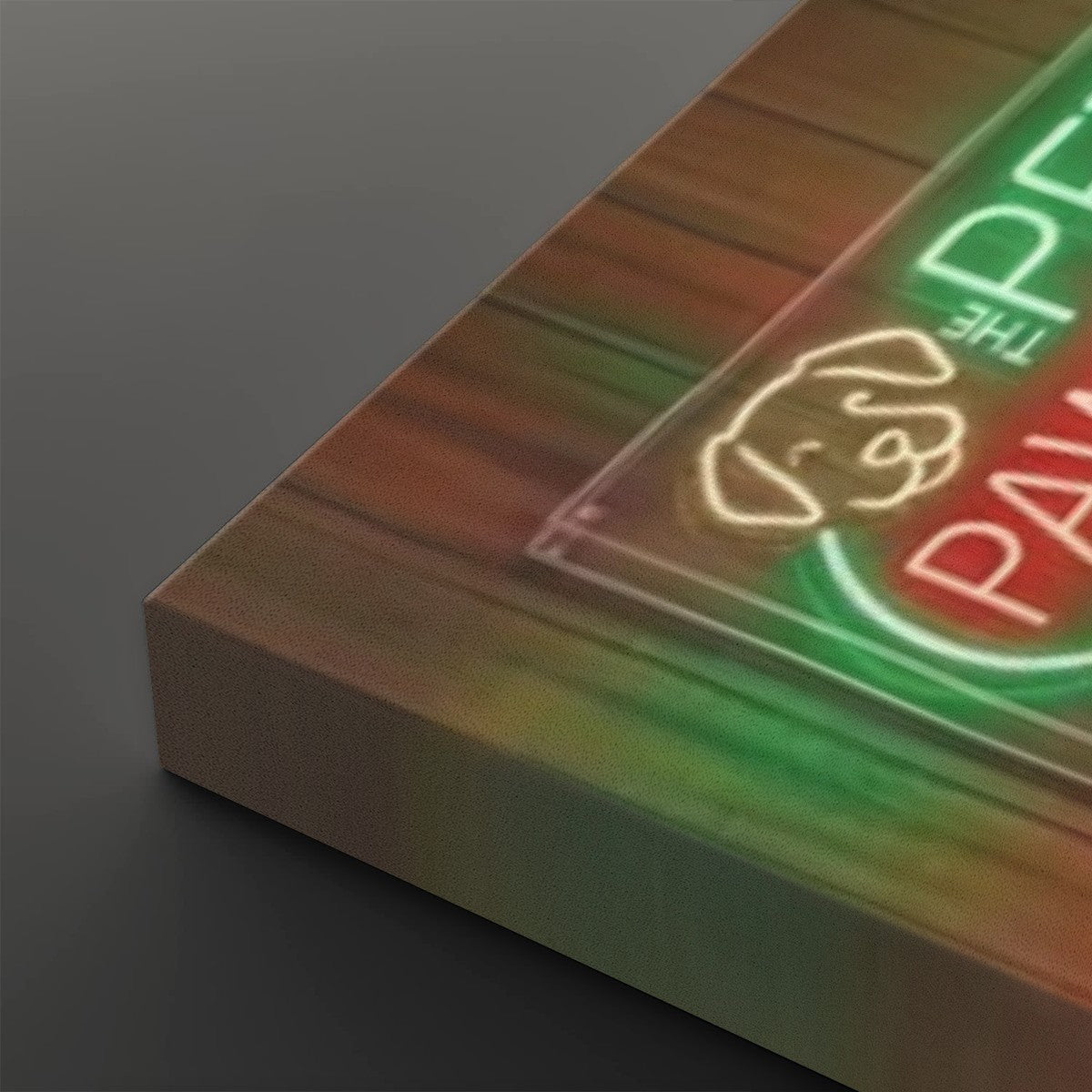 A close-up angled view of a rectangular canvas or print with a faux neon sign design. The artwork shows glowing green and red lettering reading "The Palm" with a white outline dog face, over a warm brown wood-grain background, set against a dark gray studio background.