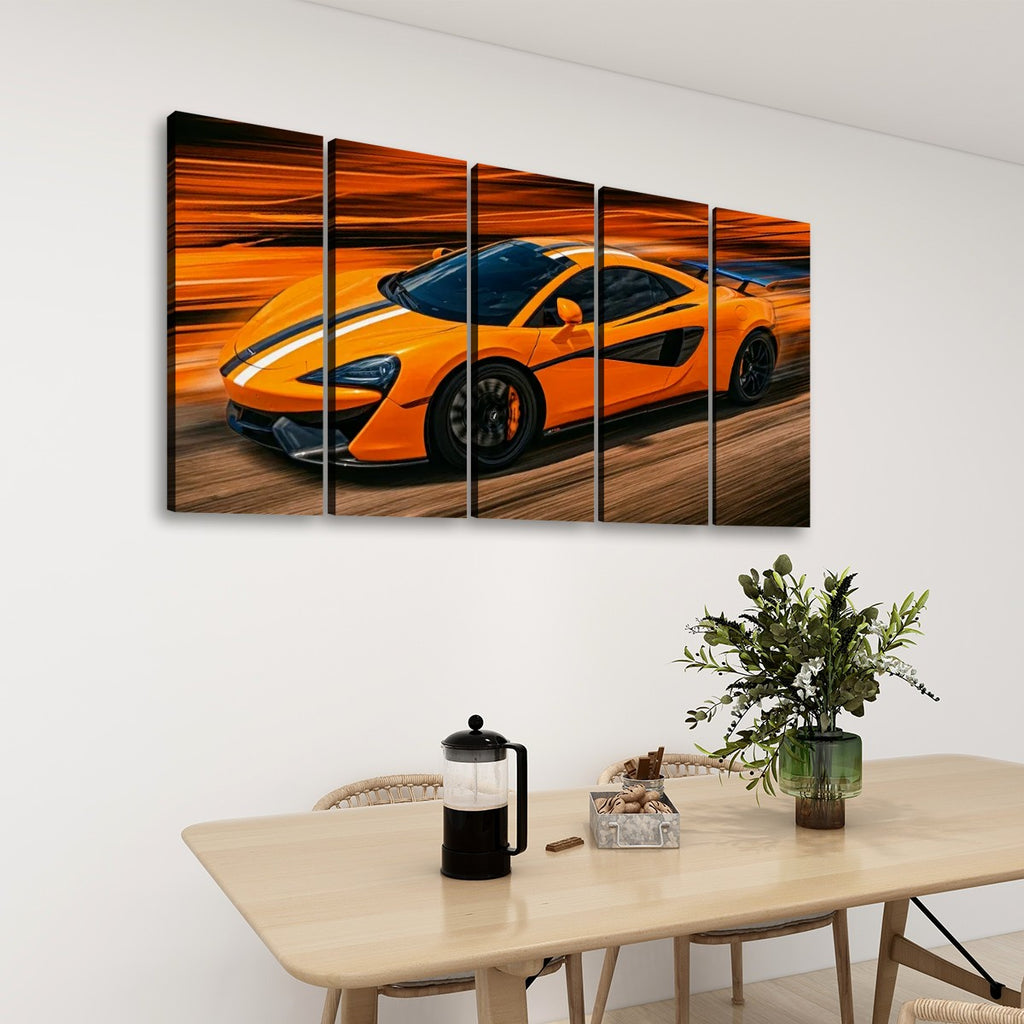 A five-panel canvas wall art set depicting a bright orange  McLaren  sports car in motion, displayed on a white wall above a light wood dining table with a vase of greenery and a French press.