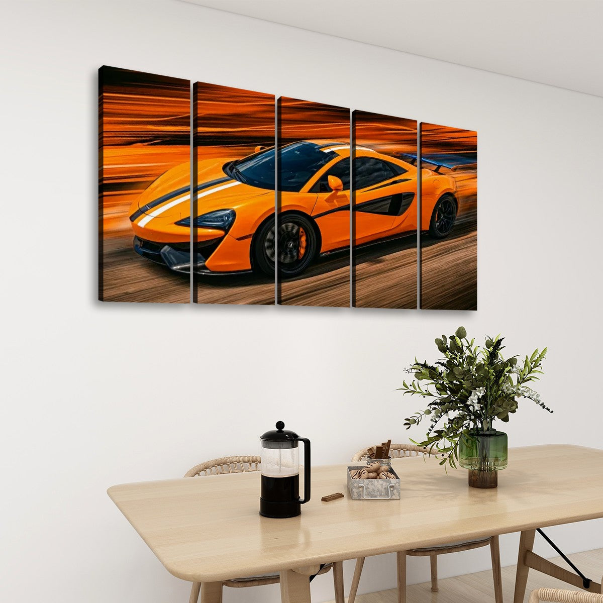A five-panel canvas wall art set depicting a bright orange  McLaren  sports car in motion, displayed on a white wall above a light wood dining table with a vase of greenery and a French press.