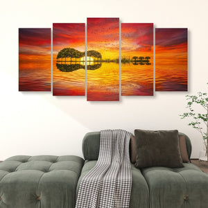 A 5-panel canvas wall art set depicting a vibrant sunset over water with a guitar-shaped island and its reflection, displayed above a green sofa in a living room setting.