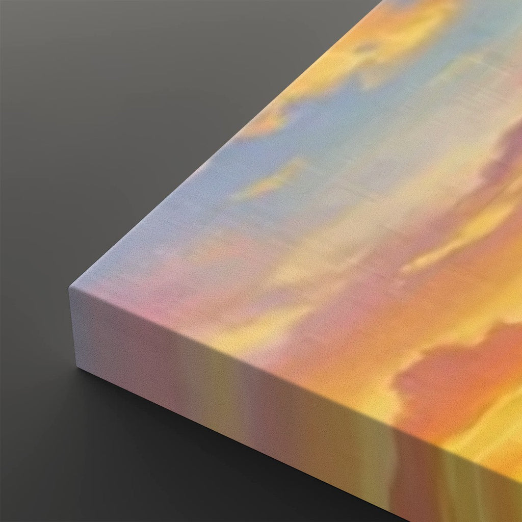 A close-up of a rectangular canvas print showing its wrapped edge, featuring an abstract sunset-like pattern in orange, yellow, pink, and soft blue tones on a dark gray background.