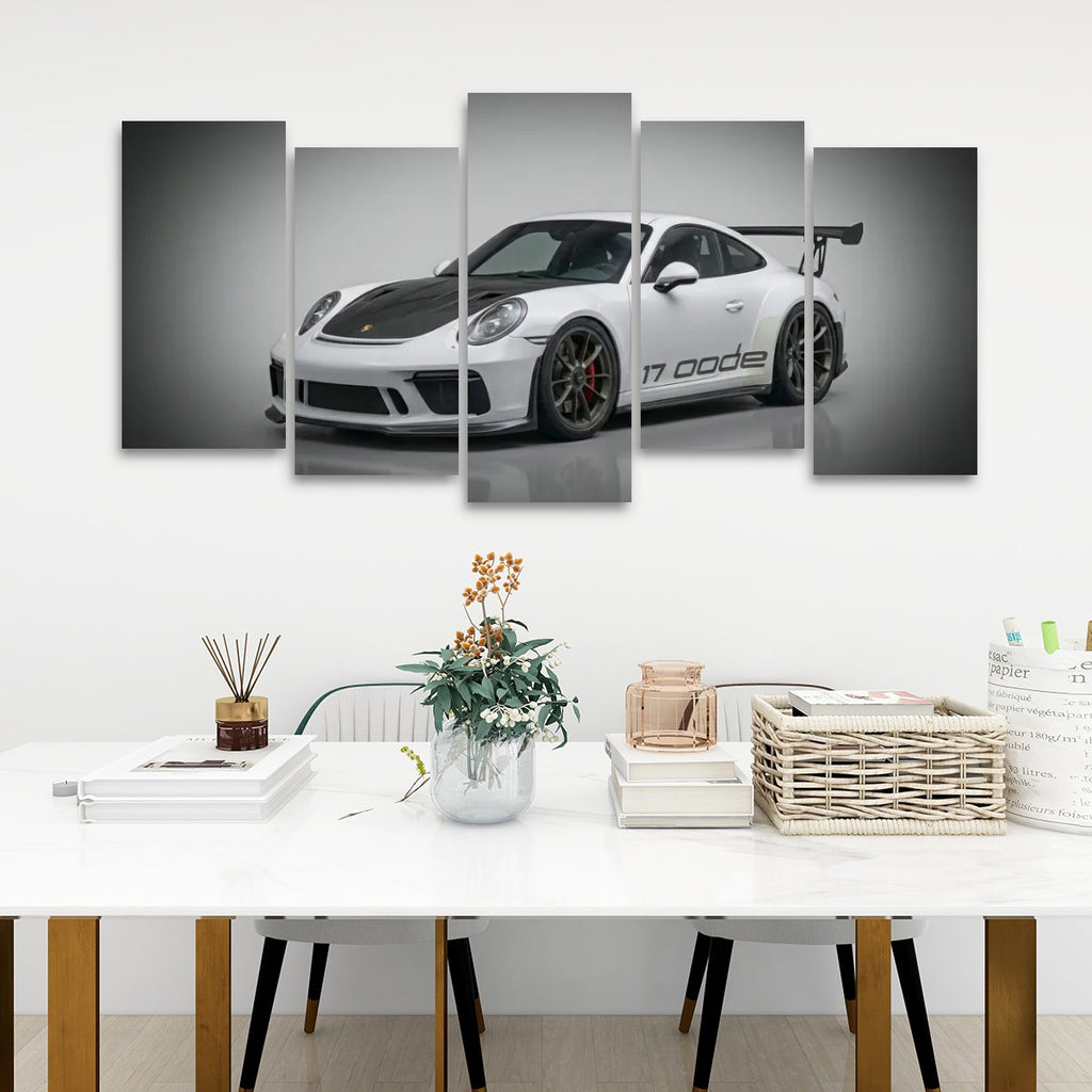 A five-panel canvas wall art print depicting a white Porsche 911 with black accents, displayed on a white wall above a styled dining table with books, a vase, and baskets.