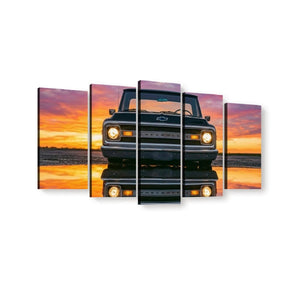 A five-panel canvas wall art set showing the front of a dark vintage 1970 Chevy C10 truck against a vivid orange and pink sunset sky, with the truck reflected in water below.