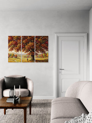 A three-panel canvas wall art set depicting a large tree with autumn foliage in a field, displayed on a light gray wall in a modern living room setting next to a white door.