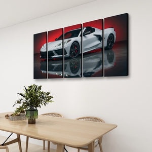 A four-panel canvas wall art print depicting a white sports car on a red and black reflective studio background, displayed above a light wood dining table in a modern room setting.