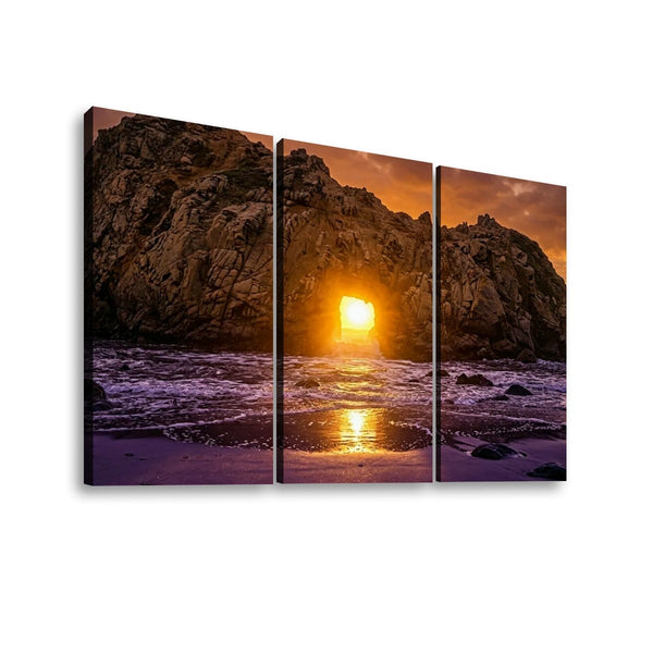 Three-panel canvas wall art showing a dramatic rocky coastline at sunset, with the sun low over the ocean and purple-toned waves reflecting on the shore, displayed against a white background.