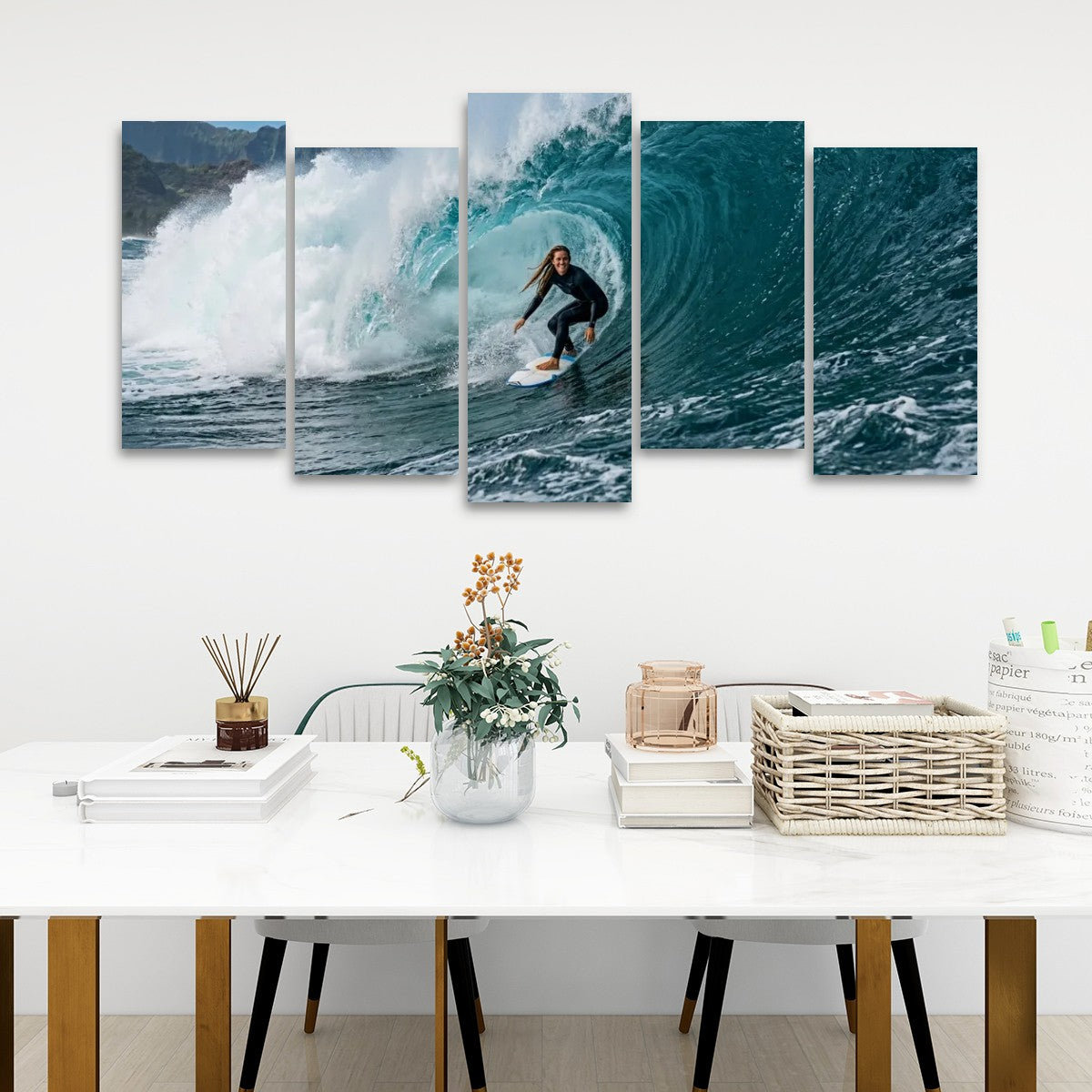 A five-panel canvas wall art set depicting a surfer riding a large turquoise wave, displayed on a white wall above a styled white table with books, a vase, and baskets.