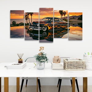 A five-panel canvas wall art set depicting a classic car with orange flames on its body, parked in front of a sunset beach with palm trees, displayed on a white wall above a styled dining table.