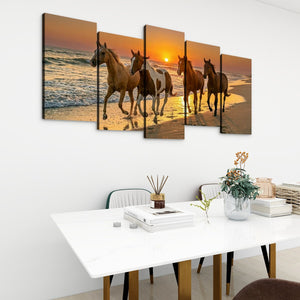 A five-panel canvas wall art set depicting horses walking on a beach at sunset, displayed above a white dining table in a modern room setting.