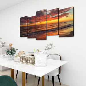 A 5-panel canvas wall art set depicting a dramatic sunset over the ocean, displayed on a white wall above a dining table in a modern, bright room.