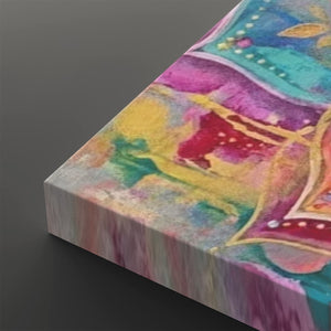 A close-up angled view of a rectangular canvas print showing an abstract painted design with blended pink, purple, teal, yellow, green, and red tones on a dark gray background.