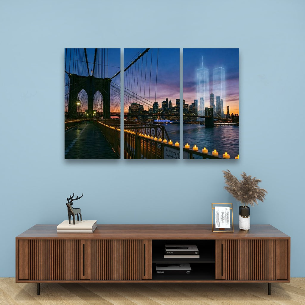 A three-panel canvas wall art set depicting the Brooklyn Bridge and New York City skyline at dusk, displayed above a wooden console table against a light blue wall.