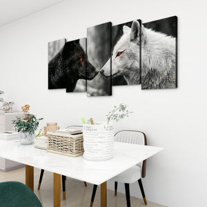 A 5-panel canvas wall art set depicting a black wolf and a white wolf facing each other, displayed on a white wall above a dining table in a modern room setting.