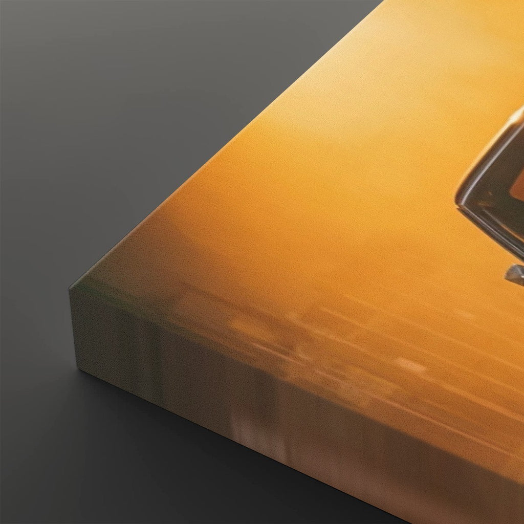 A close-up of a rectangular canvas or print showing a warm golden-orange abstract scene, photographed at an angle against a dark gray background. A small portion of a dark object is visible on the right edge.