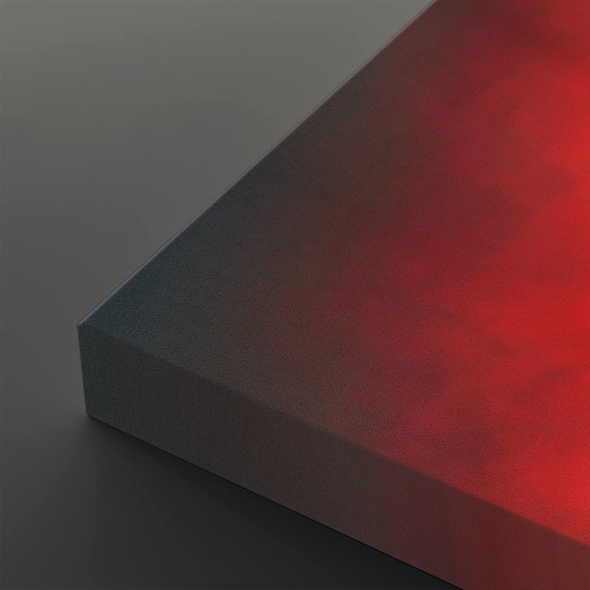 A close-up of a rectangular panel or block showing a smooth color gradient from dark gray on one side to vivid red on the other, photographed on a dark gray background.