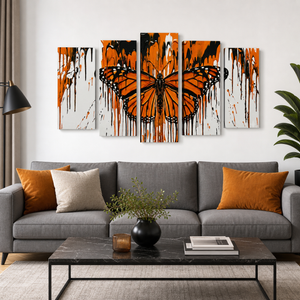 A 5-panel canvas wall art set featuring a vibrant orange and black butterfly with dripping paint effects, displayed above a modern gray sofa in a styled living room.