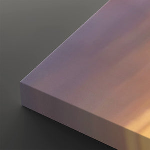 A close-up of a rectangular block with a smooth, matte iridescent surface showing a gradient of purple, pink, and warm gold tones under directional light, set against a dark gray background.