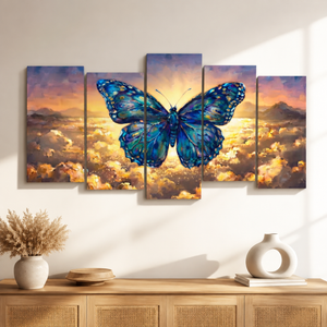 A five-panel canvas wall art set depicting a large blue butterfly over a golden sunset sky and clouds, displayed above a wooden console table with decorative vases in a styled interior setting.