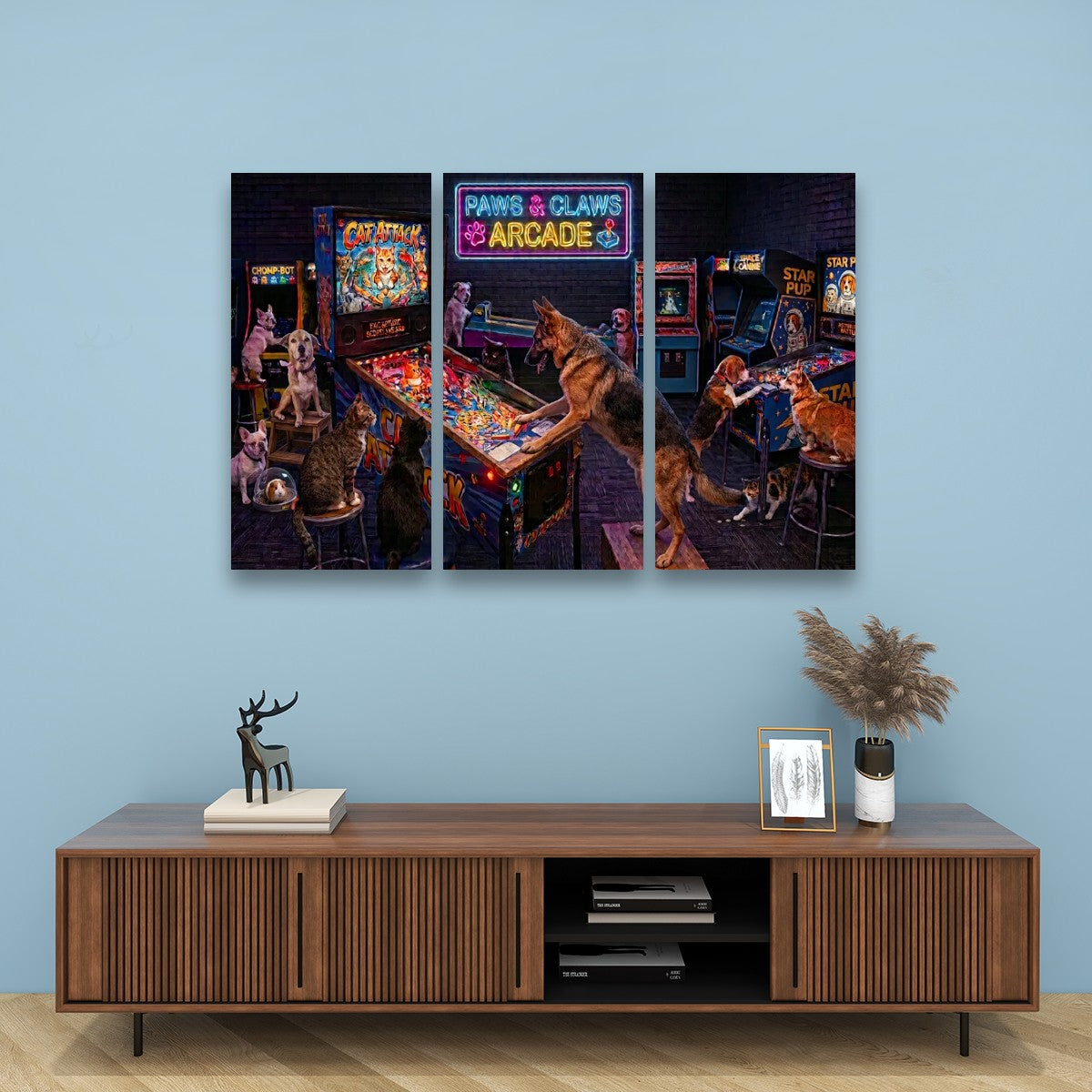 A three-panel canvas wall art print depicting dogs playing arcade games in a retro arcade, displayed on a light blue wall above a wooden console table.