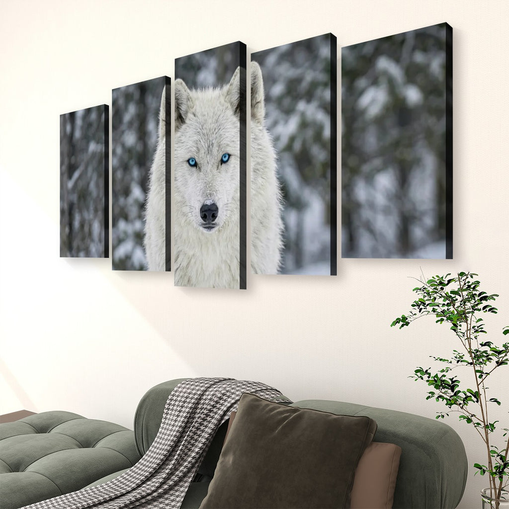 A five-panel canvas wall art set depicting a white wolf with bright blue eyes in a snowy forest, displayed on a beige wall above a green sofa with a throw blanket and a potted plant.