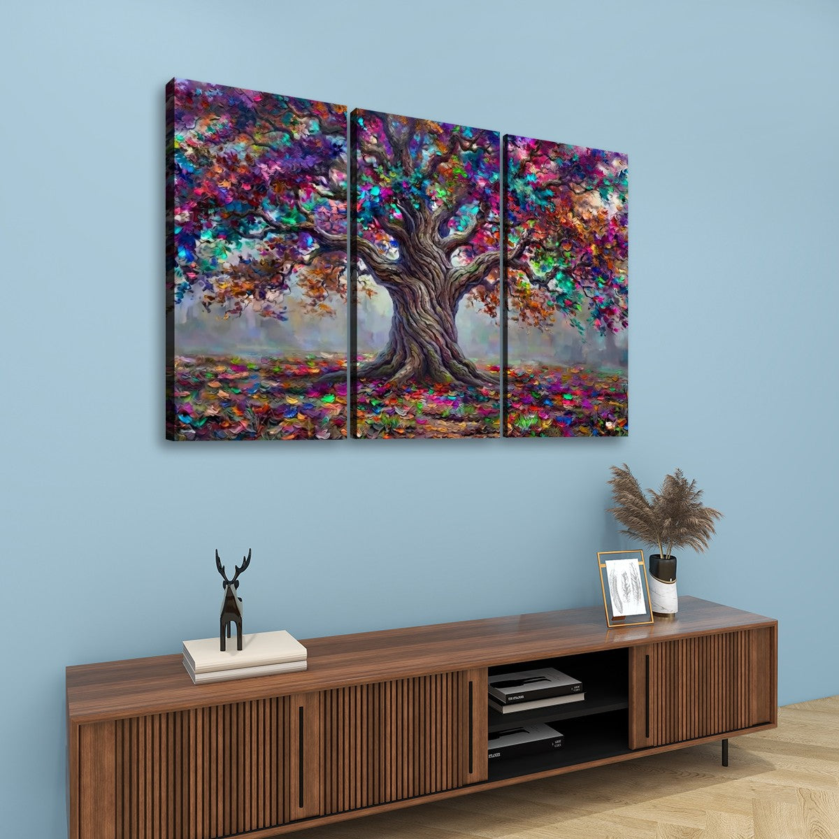 A three-panel canvas wall art set depicting a colorful, textured tree with vibrant autumn foliage, displayed on a light blue wall above a wooden console table.