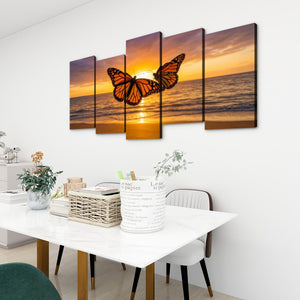 A 5-panel canvas wall art set depicting a monarch butterfly over a golden sunset ocean, displayed on a white wall above a dining table in a modern room setting.