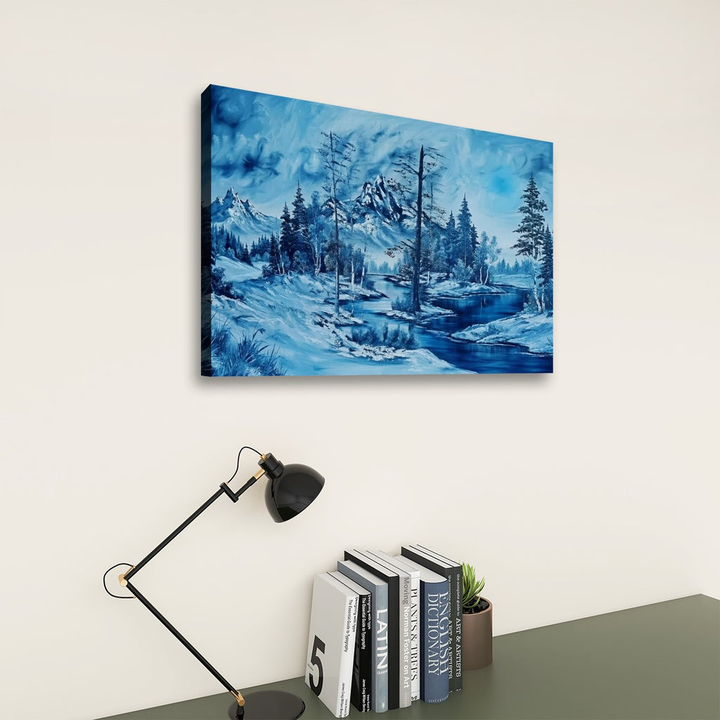 A rectangular canvas wall art print showing a blue-toned winter landscape with snowy hills, evergreen trees, and a winding river, displayed on a light wall above a desk with a black lamp and books.