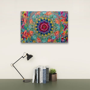 A colorful square wall art print featuring a vibrant mandala design, displayed on a light beige wall above a dark green desk with a black desk lamp, books, and a small potted succulent.