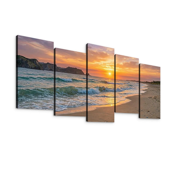 A five-panel canvas wall art set depicting a beach sunset with ocean waves, sandy shore, cliffs, and a glowing sun over the horizon, shown against a plain white background.