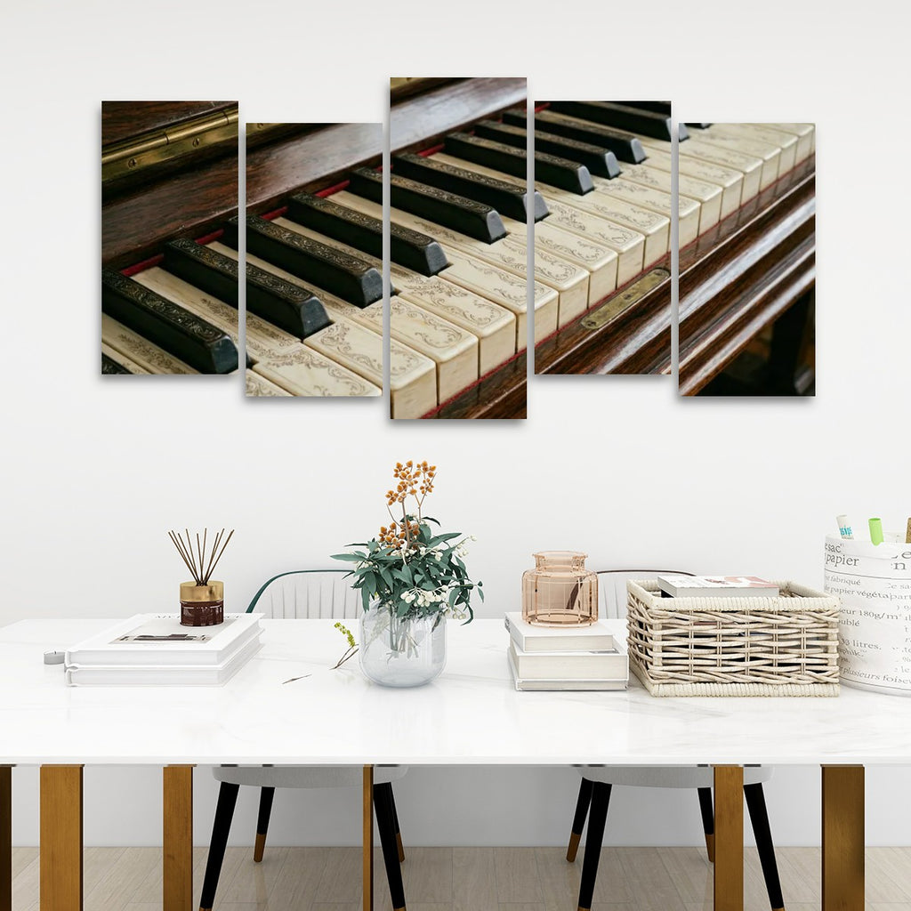 A five-panel canvas wall art set depicting a close-up of vintage piano keys, displayed on a white wall above a styled dining table with books, a vase, and chairs.