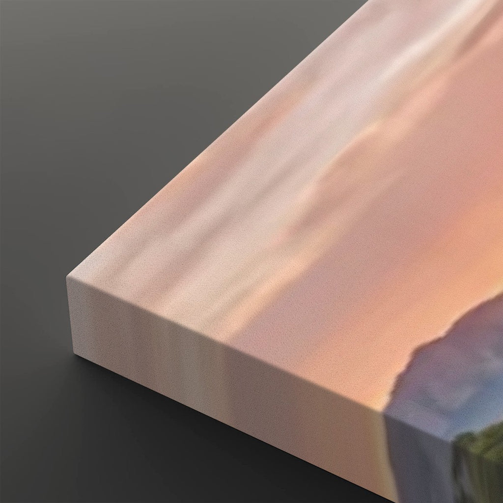 A close-up of a rectangular canvas or print showing a soft landscape scene with peach, pink, and blue tones, photographed on a dark gray background.