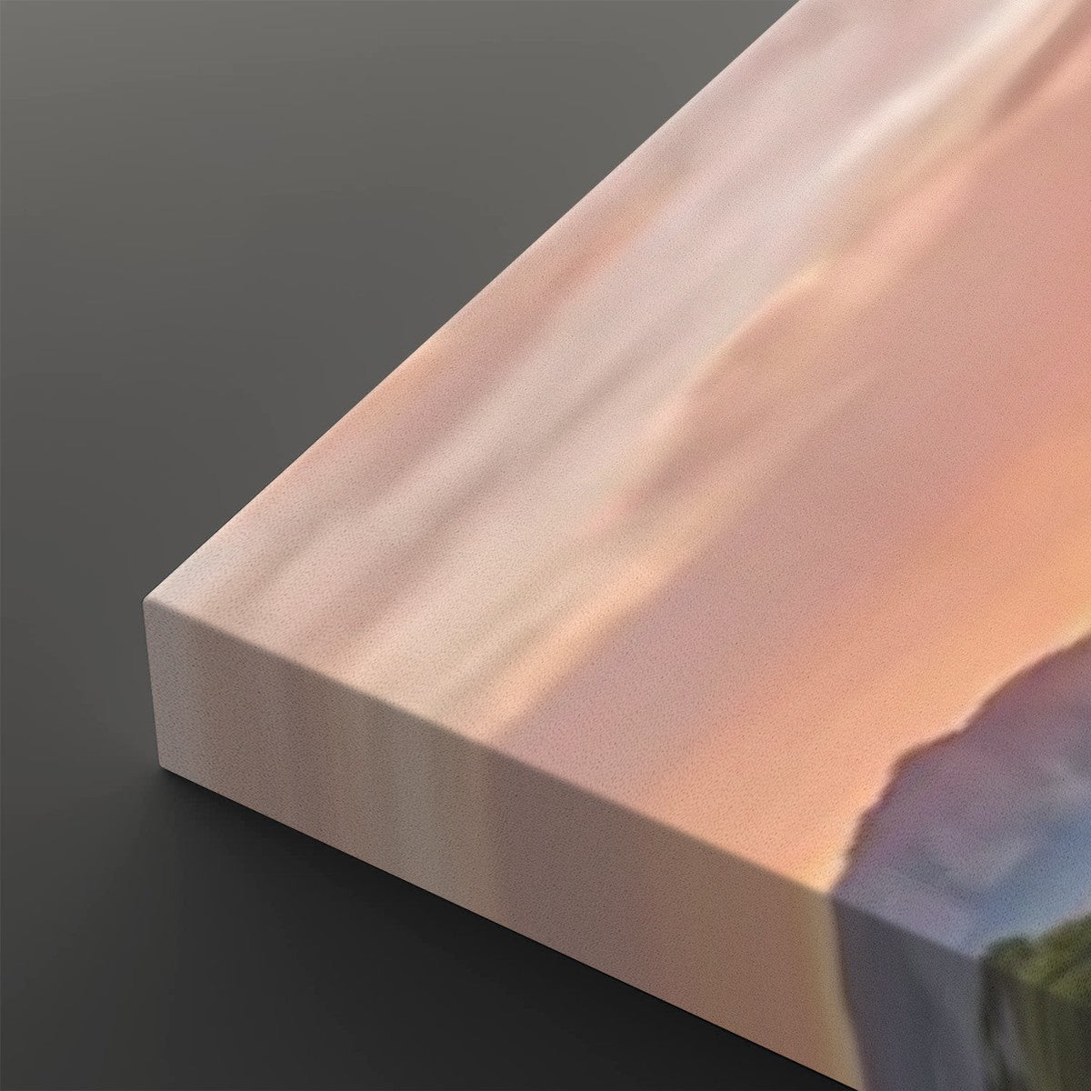 A close-up of a rectangular canvas or print showing a soft landscape scene with peach, pink, and blue tones, photographed on a dark gray background.