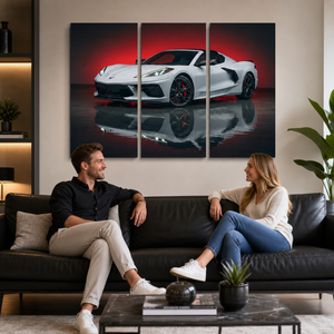 A three-panel canvas wall art print depicting a white sports car on a reflective dark surface with a red background, displayed in a modern living room above a black leather sofa where a couple is sitting and talking.