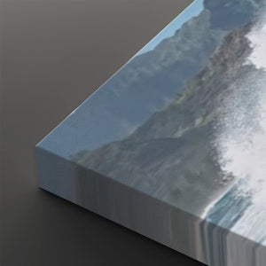 A close-up of a canvas wall art print showing an abstract coastal or mountain scene with blue-gray tones and white surf, photographed at an angle on a dark gray background.